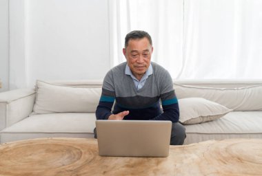 Yaşlı adam rahat bir şekilde kanepede dinleniyor, dizüstü bilgisayarı kullanmaya dalmış. Görünürde odak ve konsantrasyon rahat bir arka planda.