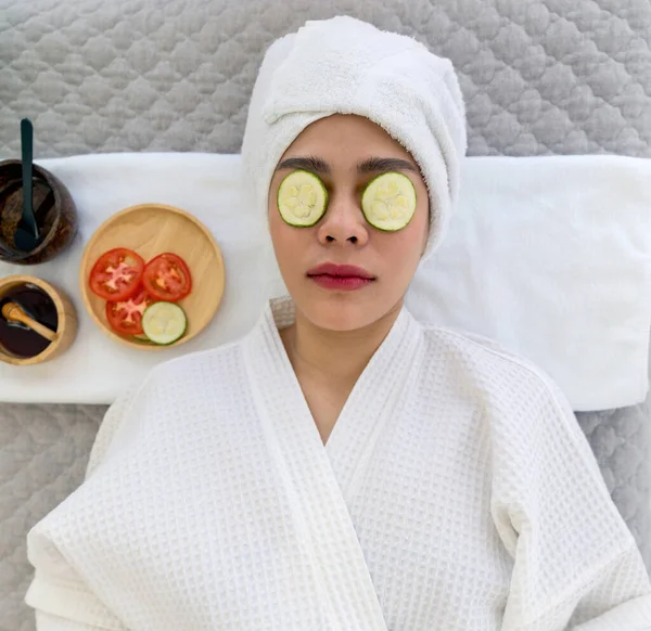 Relaxed woman enjoying a spa day with fresh cucumber slices on her eyes for under-eye rejuvenation. High angle view.
