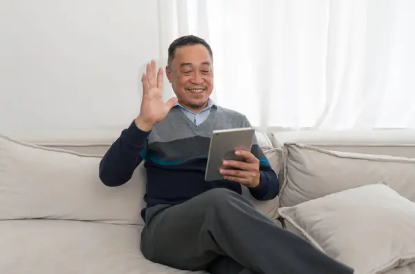 A casually dressed man sits comfortably on a plush grey couch, his attitude relaxed yet focused. His eyes are warm, inviting and fully engaged with the technology in his hand.