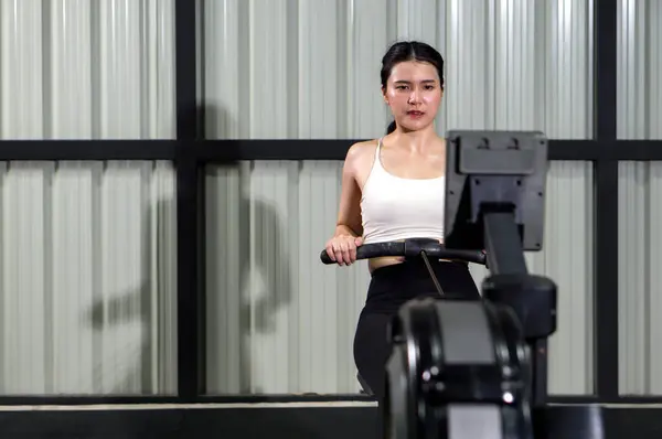 Health and active lifestyle concept. An athletic woman in sportswear is engaged in an intense workout session on a rowing machine inside a well-equipped gym.