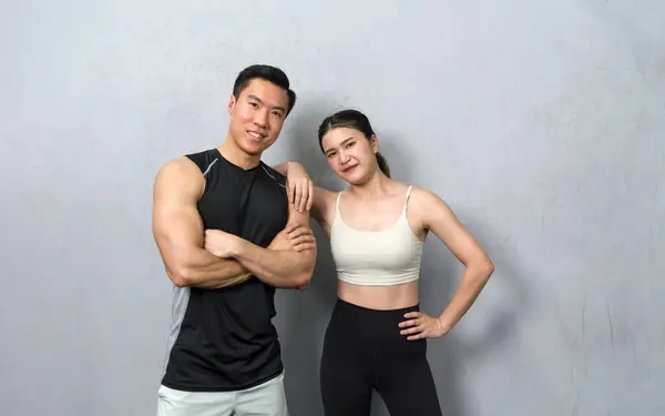 Active Asian couple showcasing their fitness goals with a captivating photo in gym. They strike a confident pose, showing their dedication to a healthy lifestyle.
