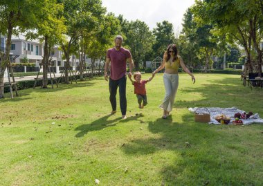 Mutlu bir adam ve kadın güneş ışığında el ele yürürler, küçük çocukları mutlu bir şekilde aralarında yürür..