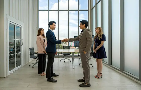 Corporate professional in formal attire engaged in a handshake during a meeting in a well-lit office space.