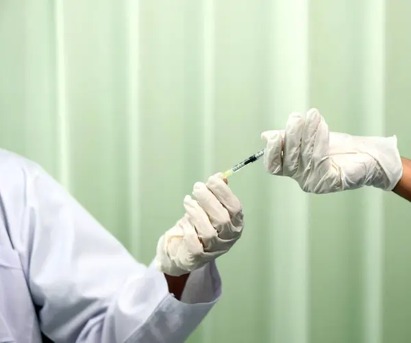 A nurse in medical gloves hands a syringe to a doctor in white gown. Closeup