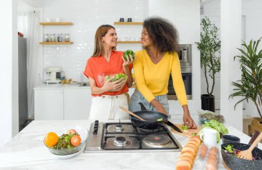 İki kadın mutfakta, birlikte yemek hazırlamak, sebze doğramak ve malzemeleri karıştırmak için mutlu bir şekilde çalışıyorlar..