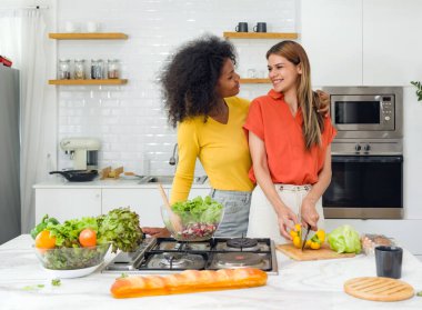 Parlak, ferah bir mutfakta iki kadın yemek pişiriyor ve malzemeleri doğruyor..
