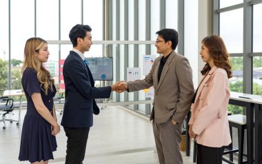 Resmi giyinmiş bir şirket çalışanı iyi ışıklandırılmış bir ofis yerinde toplantının ortasında el sıkışır..