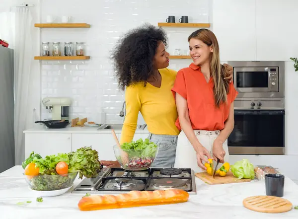 Parlak, ferah bir mutfakta iki kadın yemek pişiriyor ve malzemeleri doğruyor..