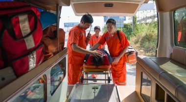 Turuncu üniformalı bir grup erkek hemşire, bir boyun ve kafa kazası kurbanını ambulansla bir yatağa yerleştiriyor..
