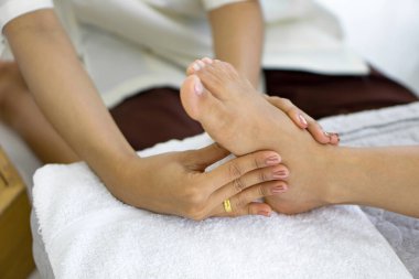 Bir insan havluyla başka bir insana ayak masajı yapıyor. Tayland masajı ile vücut bakımı.