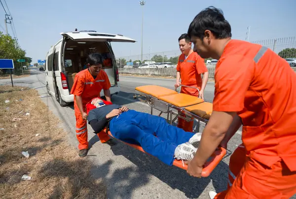 Group of paramedic or emergency medical technician (EMT) in orange uniform helping neck and head accident victim lying on stretcher long spinal board. Urgent assistance during road accident.