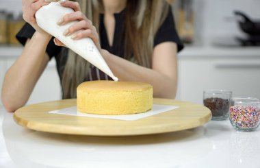 Süngerli kekin üzerine beyaz krema dökerek yuvarlak, açık renkli bir pastanın üzerine yerleştirilmiş dekoratif bir desen yaratıyor..