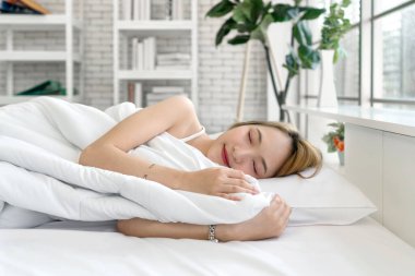 Beyaz atletli genç Asyalı kadın, uyku ve tatlı rüyalar. Parlak, rahat bir odada, yastıklı ve yorganlı bir şekilde yatıyorlar. Yan görünüm