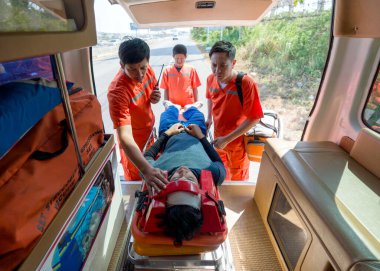 Turuncu üniformalı sağlık teknisyeni (EMT) bir grup sağlık görevlisi, bir boyun ve kafa kazası kurbanını ambulansla bir yatağa yerleştiriyor. Trafik kazasında acil yardım..