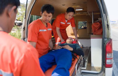 Turuncu üniformalı sağlık teknisyeni (EMT) bir grup sağlık görevlisi, bir boyun ve kafa kazası kurbanını ambulansla bir yatağa yerleştiriyor. Trafik kazasında acil yardım..