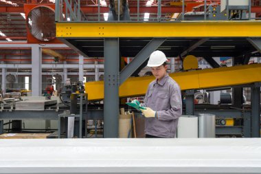 Genç Asyalı işçiler güvenlik kaskı ve eldiven takıp, etrafları makine ve malzemelerle çevrili vazifeleri kontrol ediyorlar. Metal levha fabrikasında atmosfer çalışması.