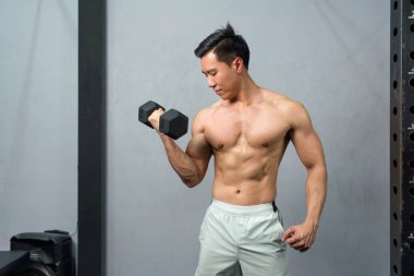 Modern bir spor salonunda fiziksel olarak formda bir adam güç ve sağIık için çabalarken ağır bir dambılı kaldırmaya kararlı..