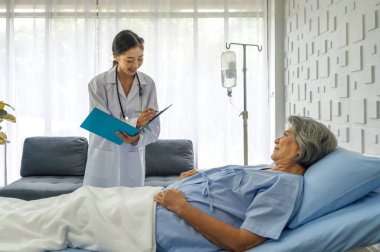 Young asian doctor in white gown with stethoscope and document folder, examine the symptom of the elderly patient in the recovery room. Healthcare and medicine concept