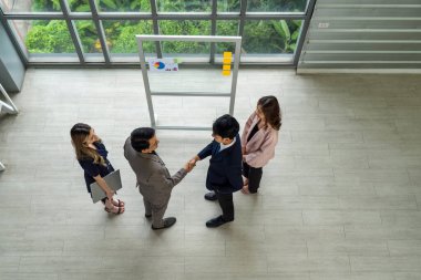İş ortakları büyük bir cam pencerenin önünde el sıkışıyor, iş yerlerinde birlik ve hırs gösteriyorlar..
