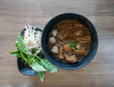 Kara soya soslu Tayland usulü etli şehriye turşulu soya peyniri ve köfte, tendon ve haşlanmış şiş ile servis edilen baharat çorbası. Taze sebzeler masada..