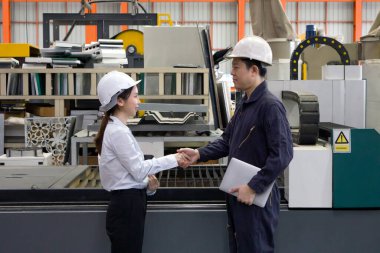 İki işçi bir fabrikada el sıkışıyor. Lazer kesici üreticisinde Yüksek Hassas Fiber Kesme Makinesi 'nin önünde güvenlik başlığı takıyorlar.