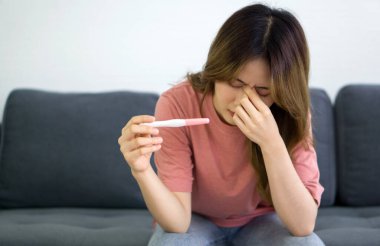 Genç Asyalı gençler oturma odasındaki kanepede oturup hamilelik testi malzemelerini tutarken strese girdiler..