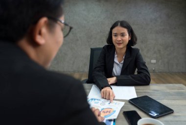 İki profesyonel şık bir ofiste odaklanmış bir sohbete girişiyor. Bir kişi belgeyi sunarken diğeri dikkatle dinliyor, işbirliği ve stratejik planlamayı gösteriyor.