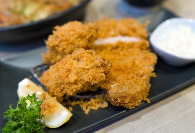 Kızarmış istiridye ve fileto katsu seti bir kase pirinçle birlikte siyah tabakta servis edilir.