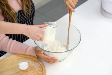 Mutfakta iki kadın tatlı yapıyor. Beyaz kek hamuru veya krema karışımı karıştıran bir kişi. Diğeri temiz bir cam kaseye taze süt döküyor..