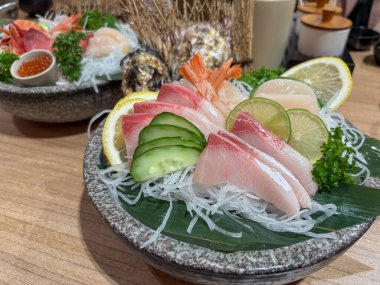Japon restoranındaki ahşap bir masada servis edilen çeşitli balık ve süslerle taze sashimi tabağı.