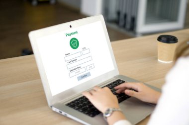 Bir kişi bir kafede online ödemeyi tamamlıyor, dizüstü bilgisayarda yazıyor. Atmosfer yakınlarda bir kahve fincanı ile rahatlıyor. Bu da gayriresmi ama verimli bir çalışma alanı olduğunu gösteriyor..