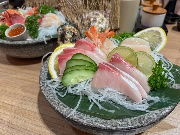 Japon restoranındaki ahşap bir masada servis edilen çeşitli balık ve süslerle taze sashimi tabağı.