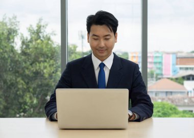 Takım elbiseli profesyonel bir adam büyük bir masada oturuyor ve dikkatle bir dizüstü bilgisayar üzerinde çalışıyor..