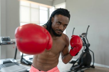 Spor salonunda sıkı çalışan kırmızı eldivenler giyen kaslı bir boksör, bir sonraki maçına hazırlanırken odaklanma ve kararlılık gösteriyor..