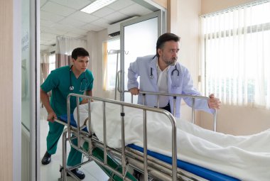 İki sağlık çalışanı, acil durum ve tıbbi bakımda takım çalışmasının bir göstergesi olarak, gün boyunca parlak bir hastane acil servisinde sedyeyle bir hastayı naklediyor..