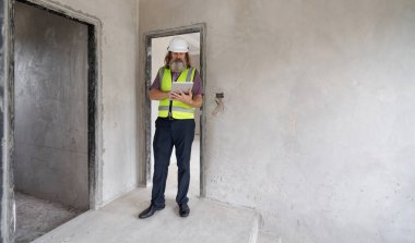 İnşaat işçisi, modern yapıda tablet kullanırken binanın tamamlanmamış iç kısımlarını inceliyor