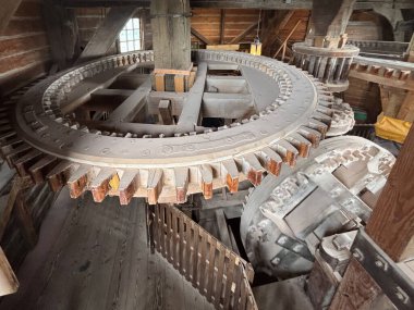 Tarihi bir yel değirmeninin içinde karmaşık ahşap teçhizat görünür. Bu da geçmişten kalma geleneksel işçilik ve mühendisliği gösteriyor. Yumuşak akşam ışığı kırsal atmosferi güçlendirir..