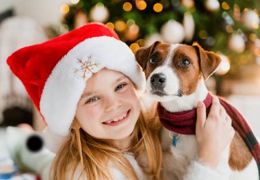 Noel ağacının yanında köpeğiyle Noel 'in tadını çıkaran tatlı küçük kız kameraya bakıyor.
