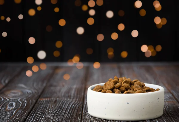 Festive background with animal food. Feed grains lie in a plate on a wooden table with Christmas lights on the background