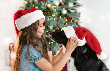 Tatlı bir genç kız köpeğiyle eğleniyor Noel ağacının yanında onu öpmeye çalışıyor.. 