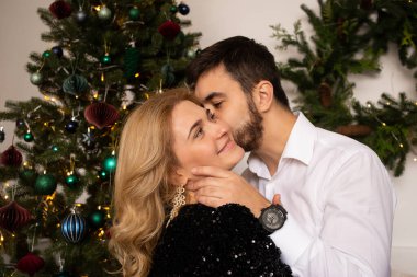 Aşk evde hediye ağacıyla yakınındaki Aralık ayında Noel arifesi öpüşme içinde genç tatlı güzel Çift.