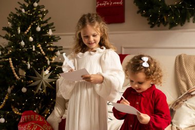 Noel ağacının yanında Noel Baba 'ya mektup yazan iki kız kardeş. Mutlu Noeller ve mutlu tatiller.