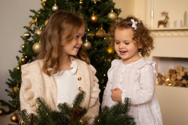 Noel ağacının yakınındaki bir odada ellerinde Noel çelengiyle genç kızlar.