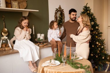 Ebeveynler ve iki kız kardeş mutfakta kurabiyeli çocuklar. Arka planda Noel ağacı.