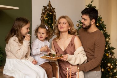 Mutlu bir aile mutfakta kurabiyelerle eğleniyor. Arka planda Noel ağacı.