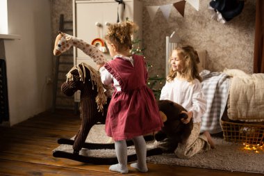 İki kız kardeş çocuk odasında, yatağın yanında oyuncak hayvanlarla oynuyorlar.