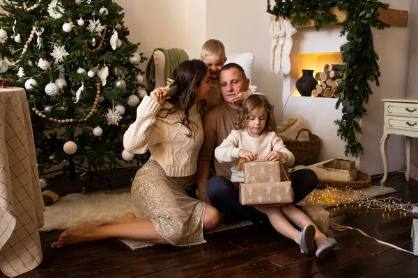 happy family in their living room, in front of the Christmas tree with presents in their hands