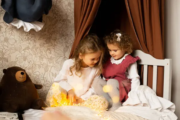 子供の部屋に座っている2人の姉妹は おもちゃの動物と一緒に自宅でベッドで一緒に時間を過ごします ストック写真