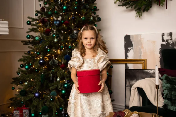 ギフトボックス付きのクリスマスツリーの近くに立っているドレスの小さな女の子 ストックフォト