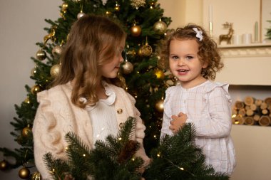 Noel ağacının yanında ellerinde Noel çelengiyle evde genç kız kardeşler.